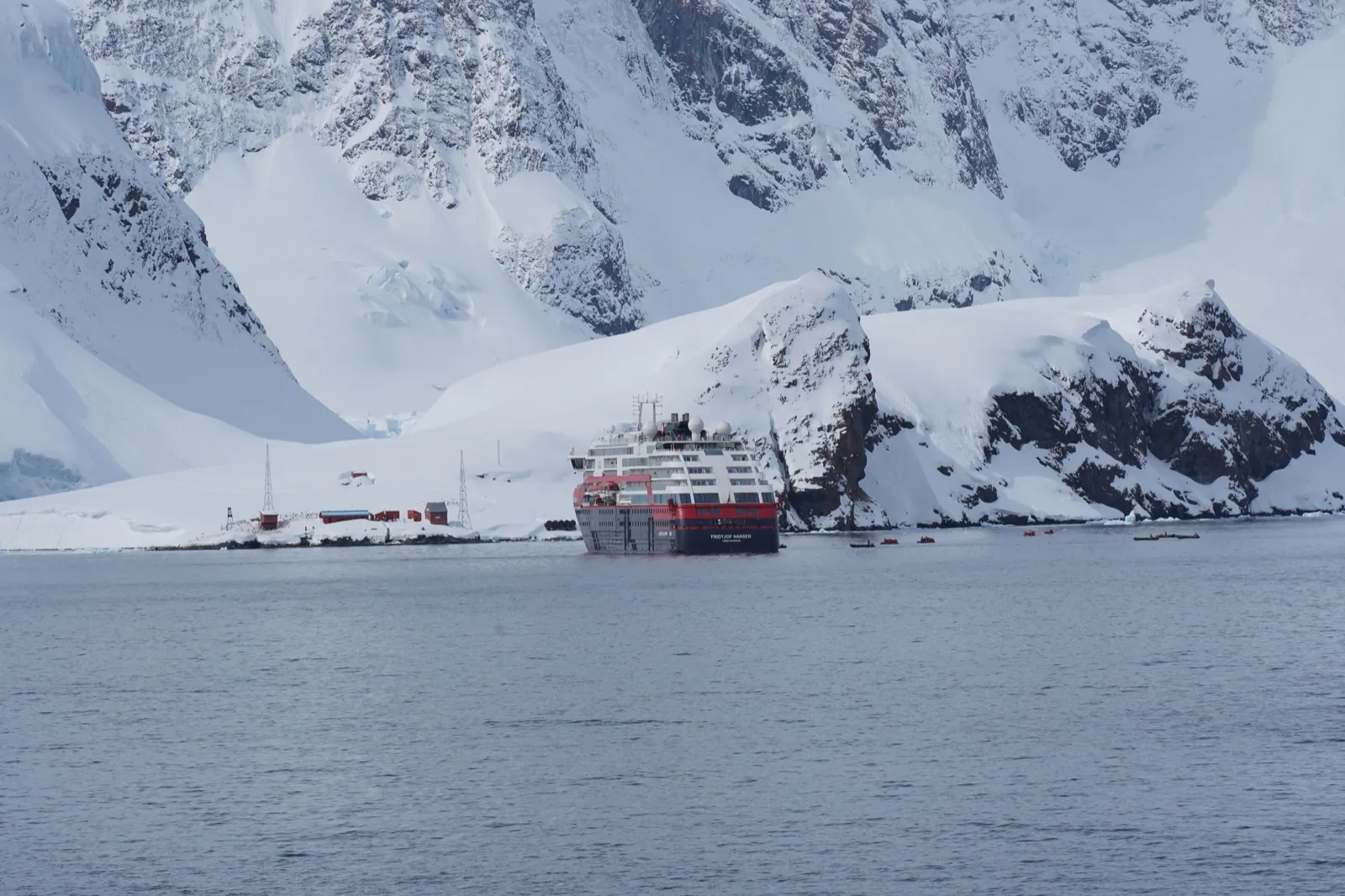 A polar expedition vessel dwarfed by snow-covered mountains in Antarctica