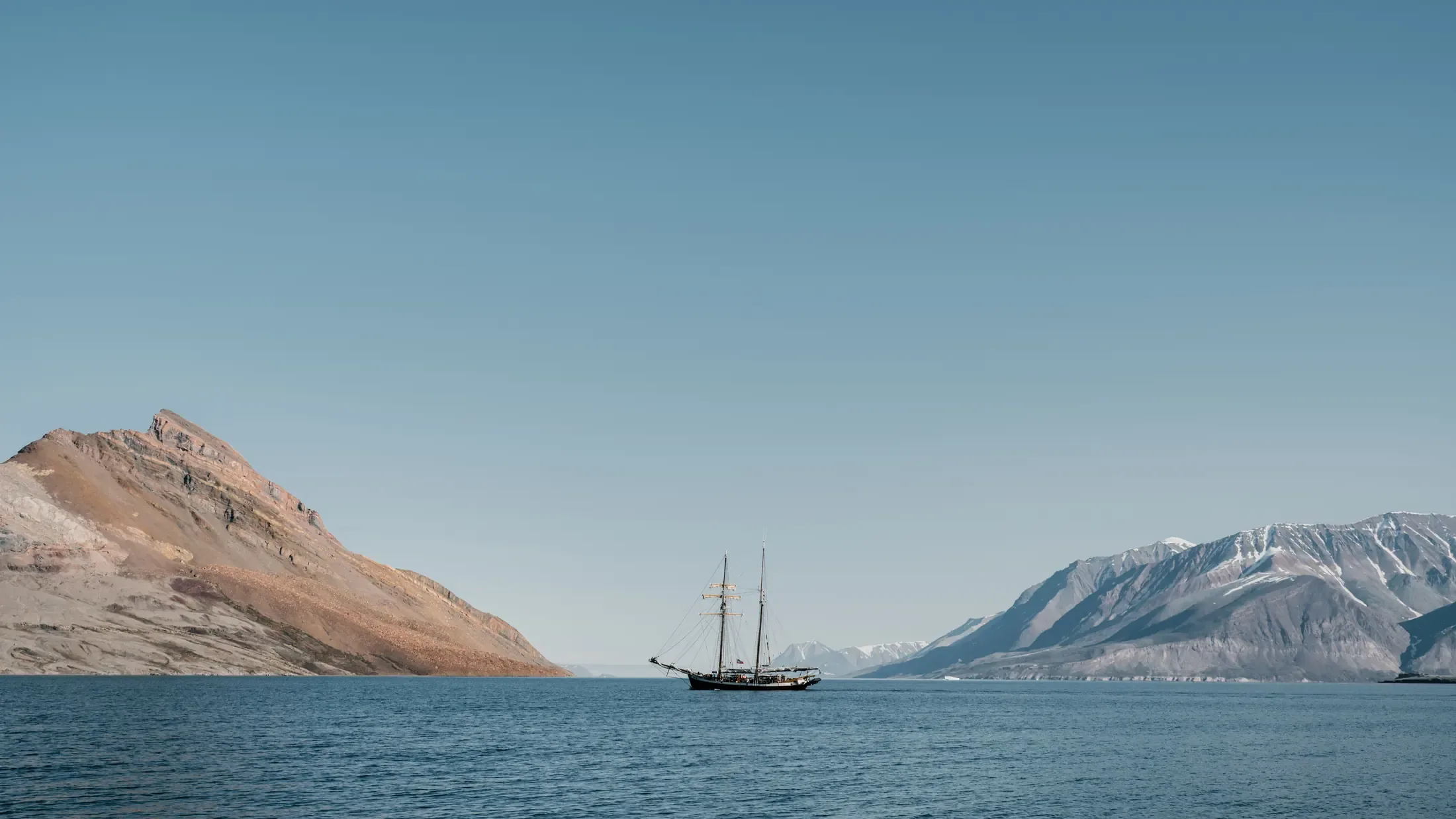 A classic sailing vessel at anchor in an Arctic fjord beneath snow-covered ridges