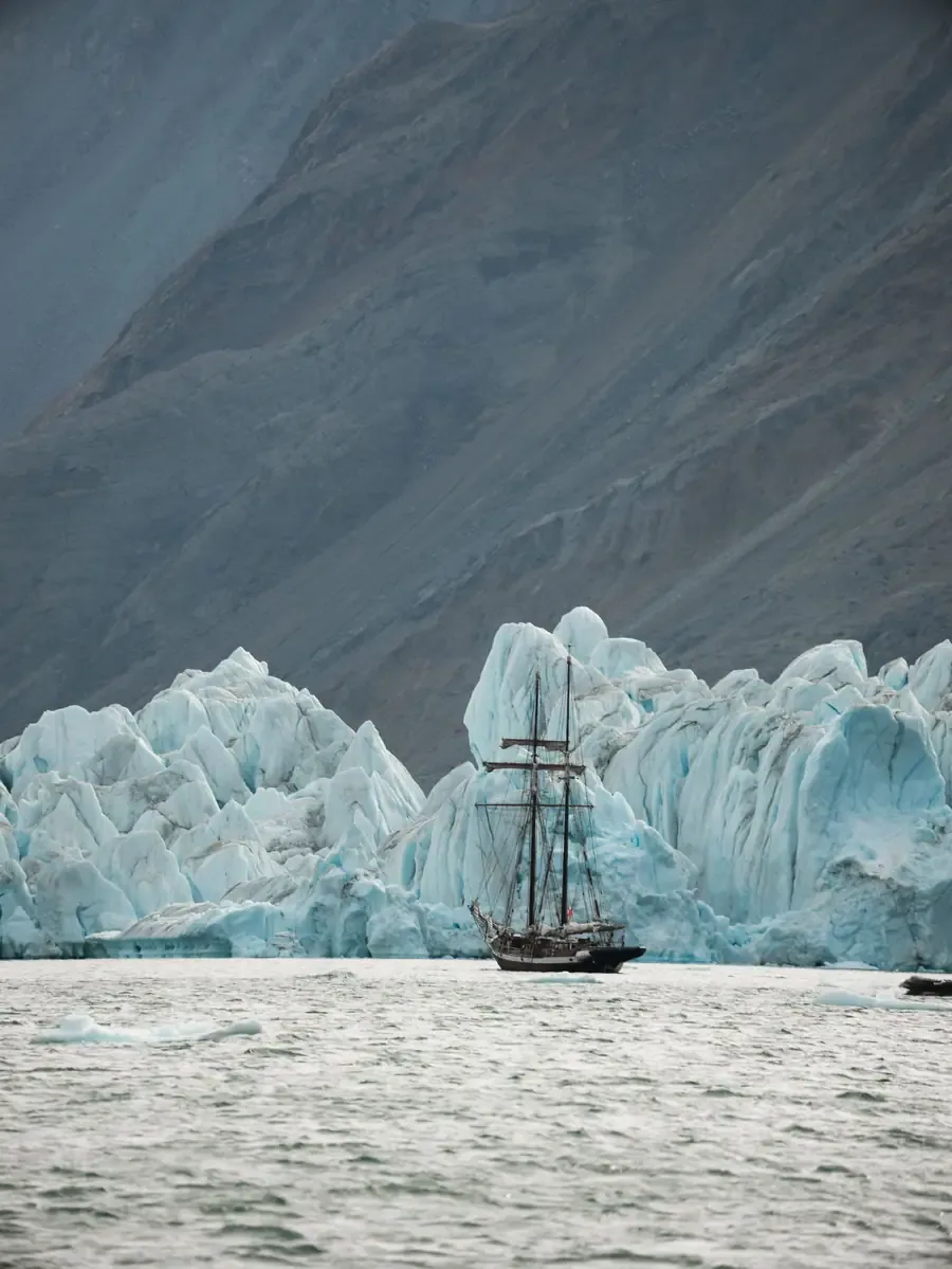 A tall ship beneath towering glacier ice